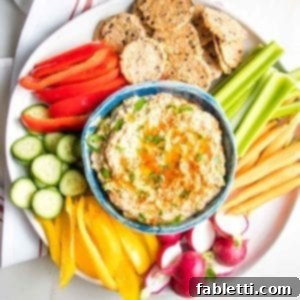 Velvety Roasted Garlic and Tahini Baba Ganoush 13 Blue bowl filled with Roasted Eggplant Dip sprinkled with parsley and paprika on top of a white plate with brightly colored veggies for dipping.