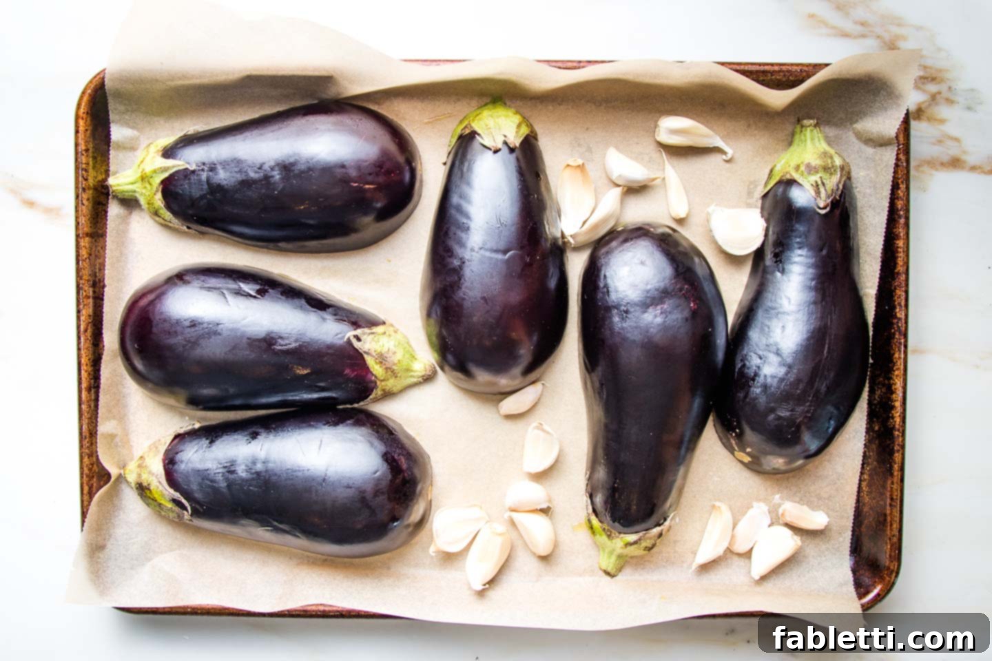 Velvety Roasted Garlic and Tahini Baba Ganoush 4 Halved eggplant and garlic cloves with their skins on a parchment lined baking tray.