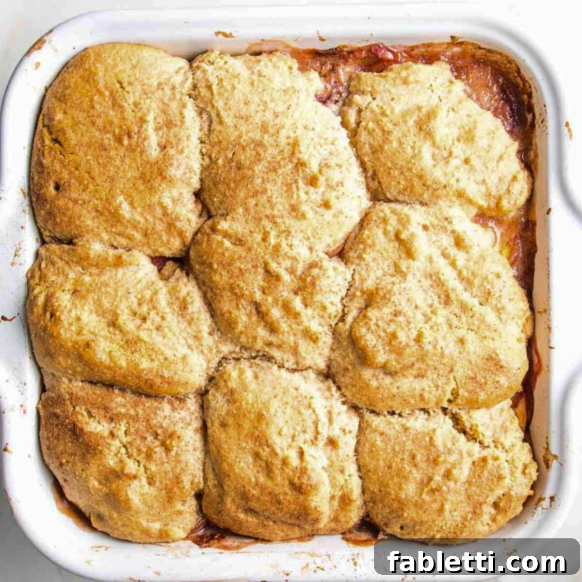 A vegan peach cobbler in a square baking dish, freshly baked and golden brown with bubbly fruit around the edges.