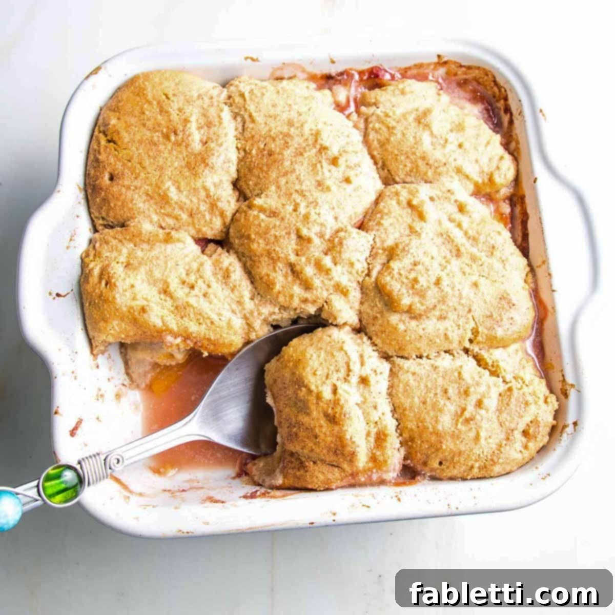 Serving peach cobbler from a baking dish onto two plates, emphasizing the jammy peaches and biscuit topping.