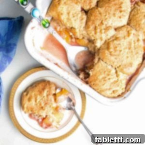 Serving of peach cobbler on a china plate with baking dish in the background, inviting and delicious.