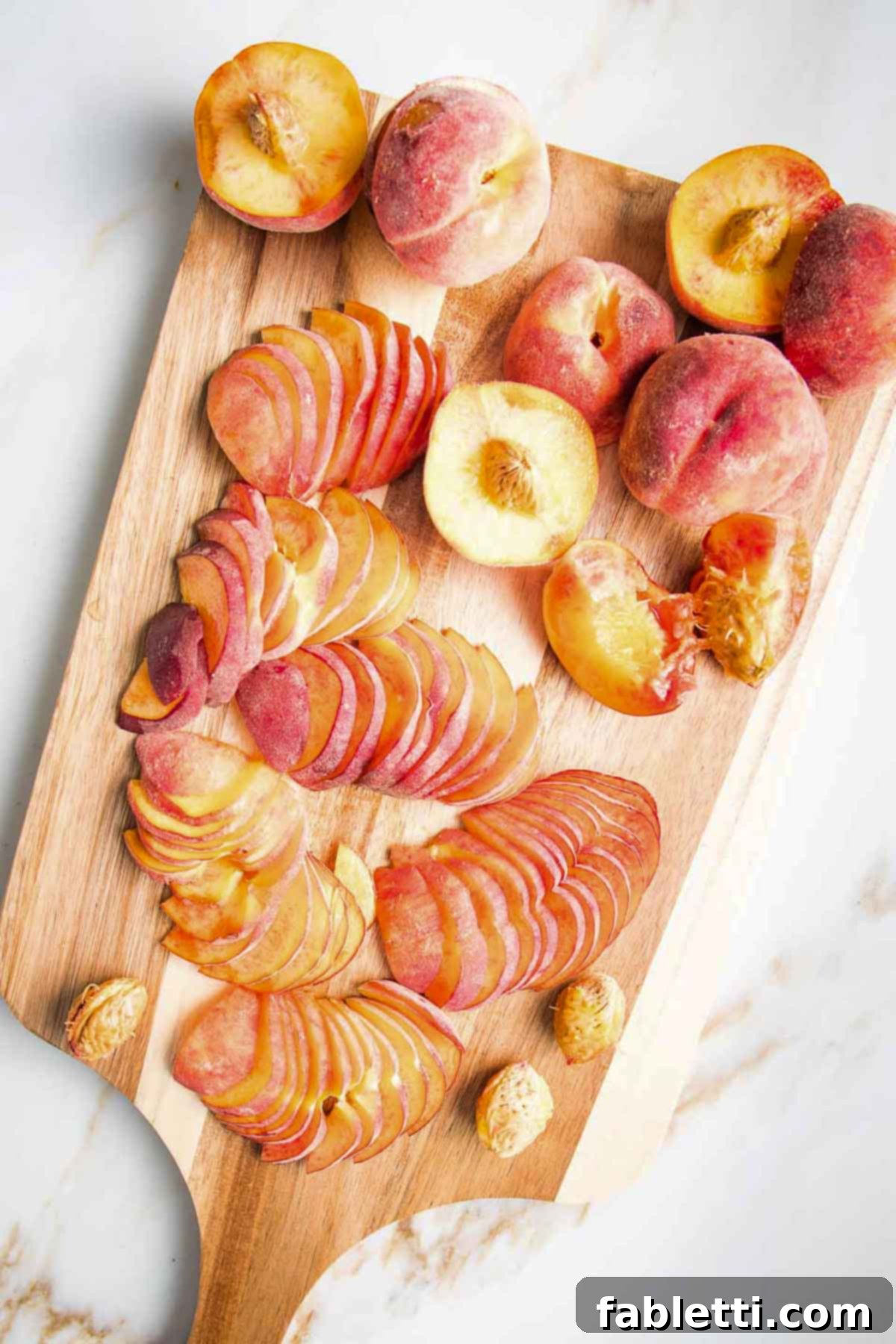Cutting board filled with halved peaches, some sliced thin, some with pits removed, showcasing the prepared fruit.