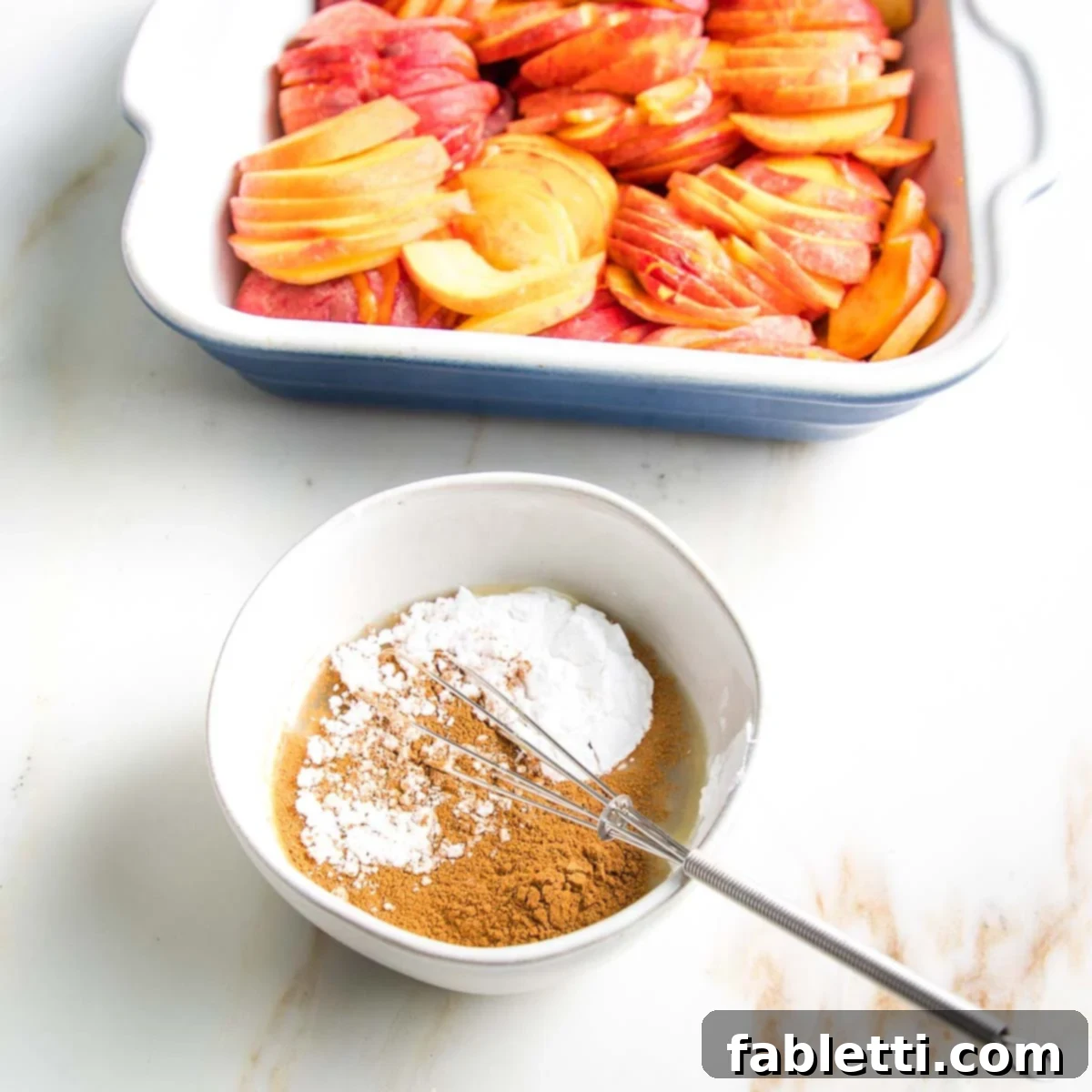 Bowl of arrowroot powder, cinnamon, lemon juice in front of a baking dish filled with peach slices, preparing the filling.