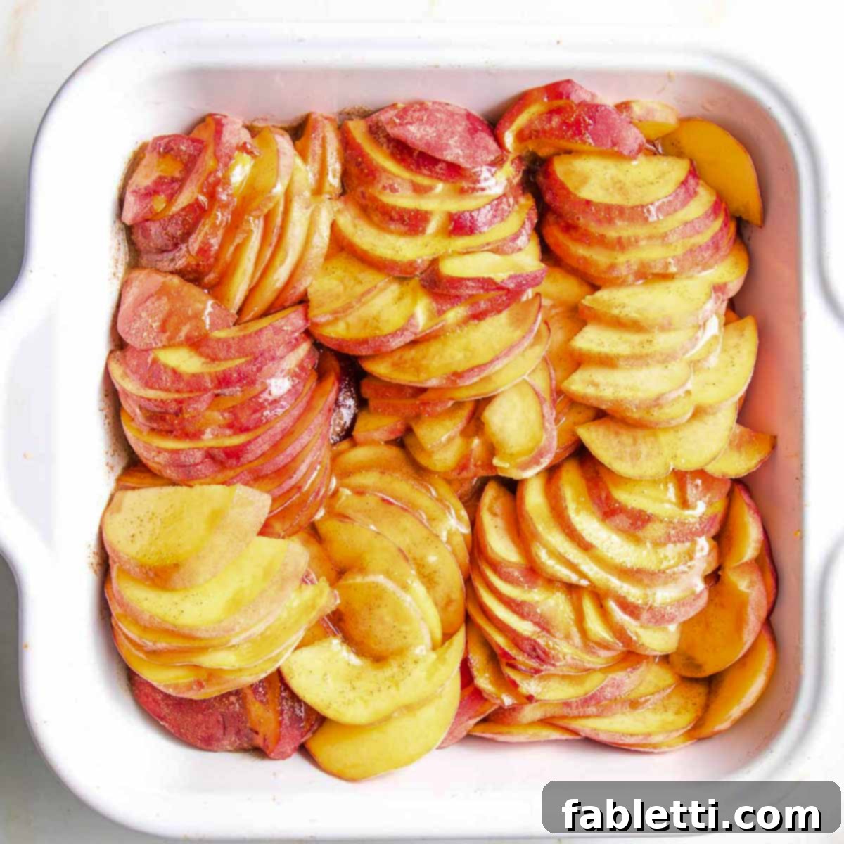 Baking dish filled with peach slices, covered with jammy lemony cinnamon mixture, ready for the topping.