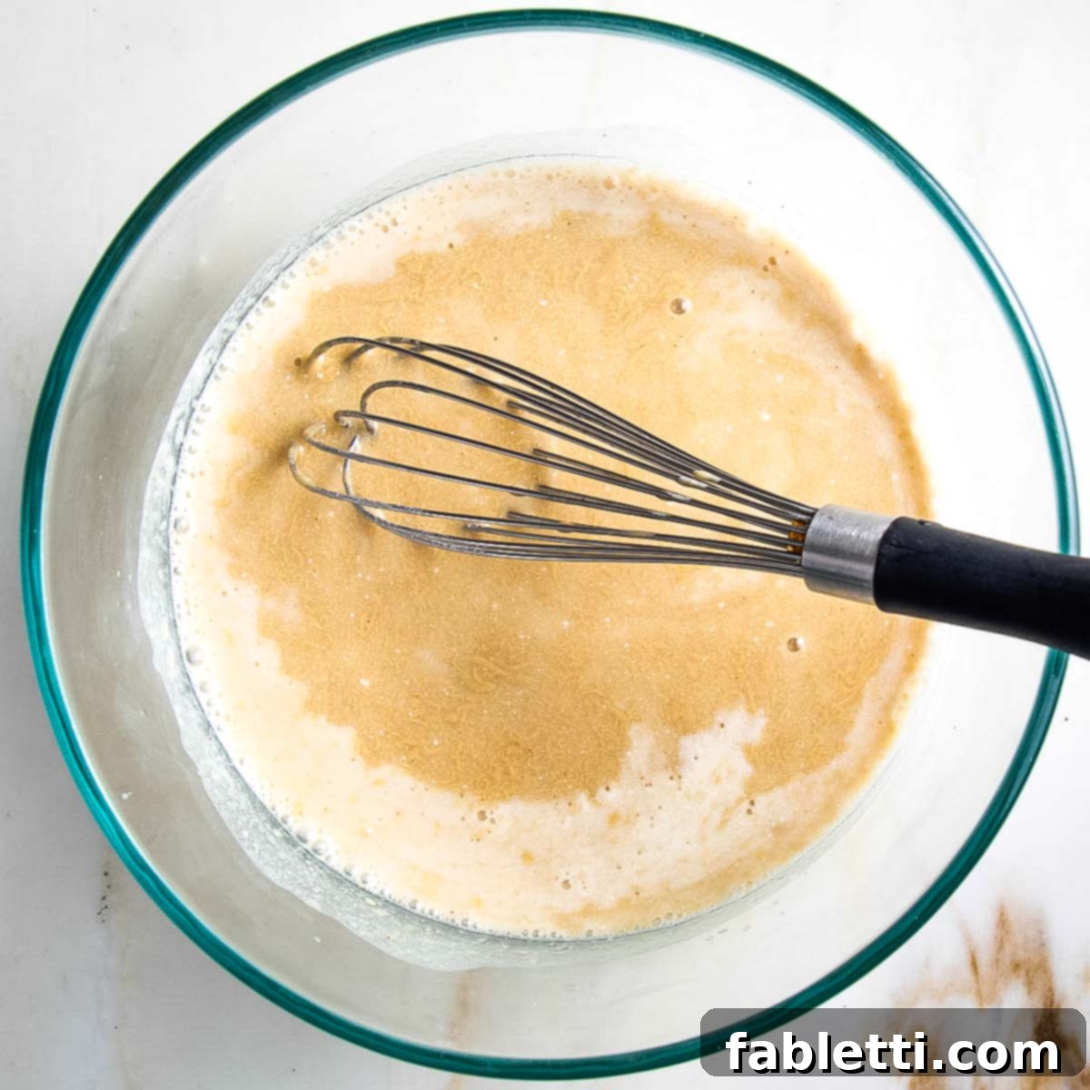 Whisking together wet ingredients for cobbler topping in a glass bowl to ensure smooth consistency.