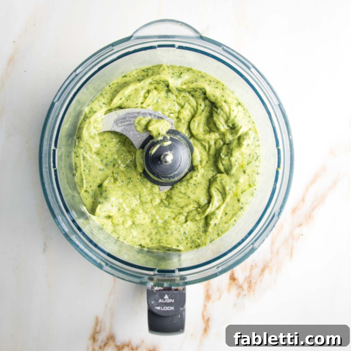 Luscious Dairy-Free Avocado Lime Dressing 5 Food processor bowl containing a perfectly smooth, creamy green avocado lime cilantro dressing, glistening and ready to be served or stored, showcasing its appealing texture.