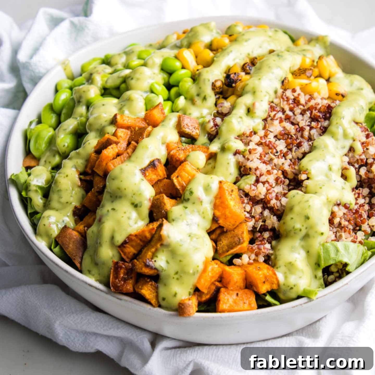 Luscious Dairy-Free Avocado Lime Dressing 8 White bowl brimming with vibrant green leafy vegetables, roasted sweet potatoes, fluffy quinoa, bright green edamame beans, and sweet corn kernels, all generously drizzled with creamy avocado lime cilantro dressing for a fresh, plant-based meal.