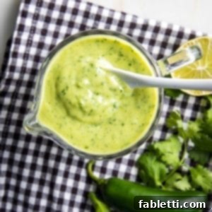 Luscious Dairy-Free Avocado Lime Dressing 9 Black and white checkered cloth with a glass pitcher filled with avocado cilantro lime dressing, plus cilantro, jalapeno and a lime on the side.