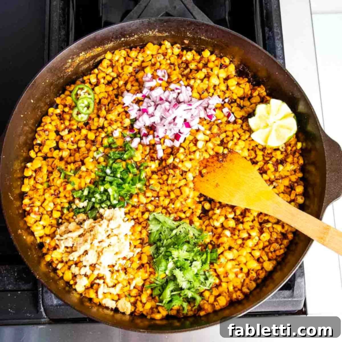 Zesty Vegan Elote 13 Cast iron skillet filled with corn, fresh herbs, onions, cooking on the stove.