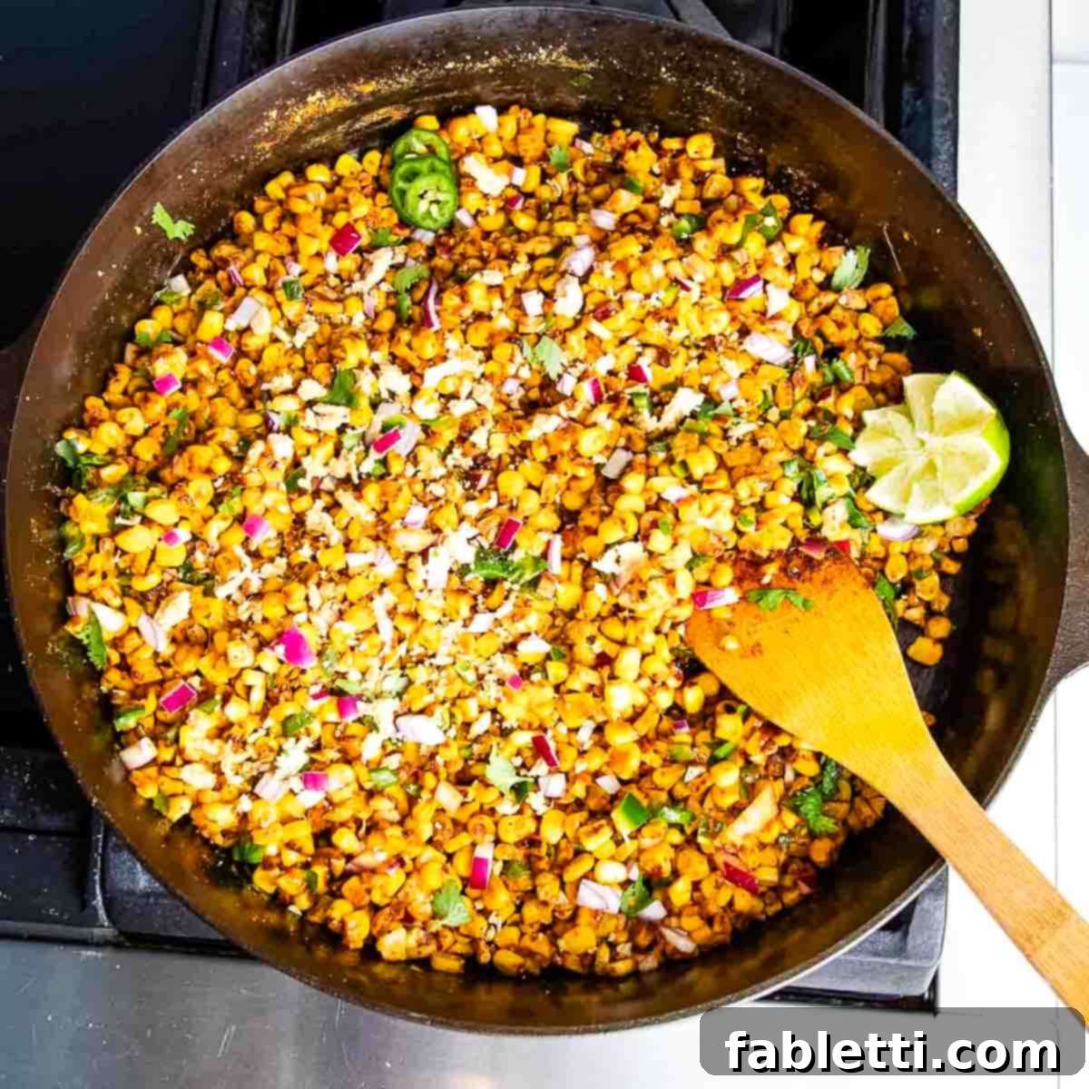 Zesty Vegan Elote 14 Skillet filled with Mexican street corn and a wooden spatula.