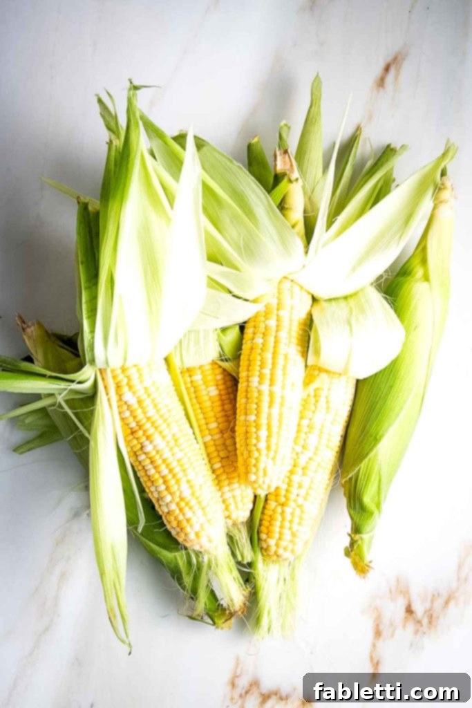 Zesty Vegan Elote 4 Fresh corn on the cob with husks pushed up.