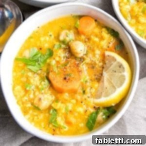 Zesty Vegan Lemon Chickpea Rice Soup 15 White bowl filled with thick chickpea soup. Bright yellow broth with chickpeas, rice, carrots, a lemon wedge, and sprinkled with chopped parsley, salt, and pepper.