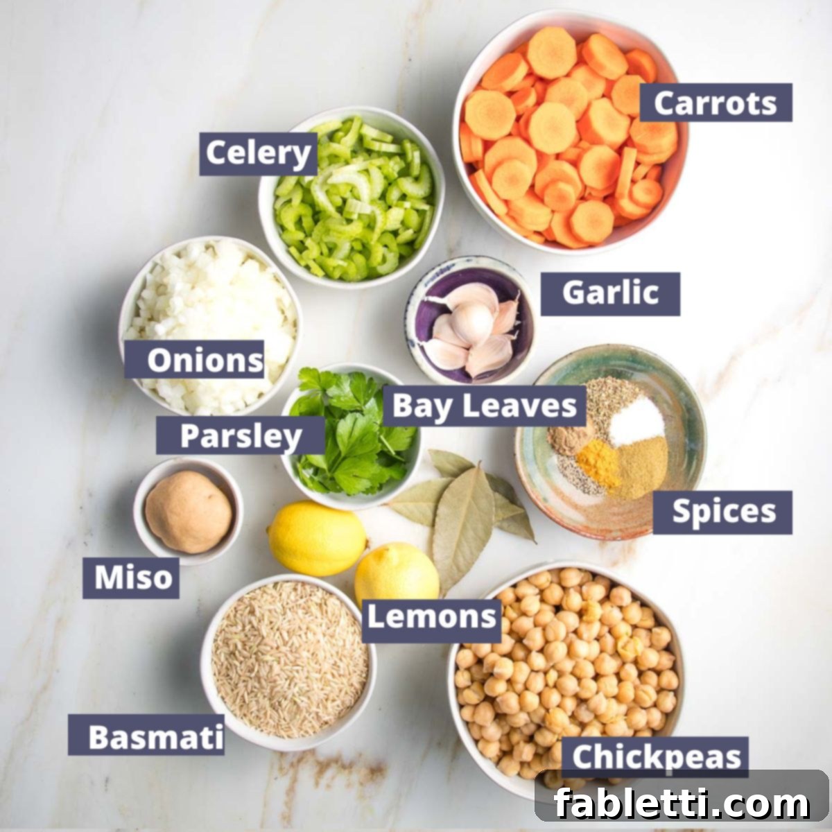 Zesty Vegan Lemon Chickpea Rice Soup 4 Labeled ingredients for chickpea soup: carrots, celery, onions, garlic, various spices, chickpeas, basmati rice, miso paste, lemons, fresh parsley, and bay leaves.