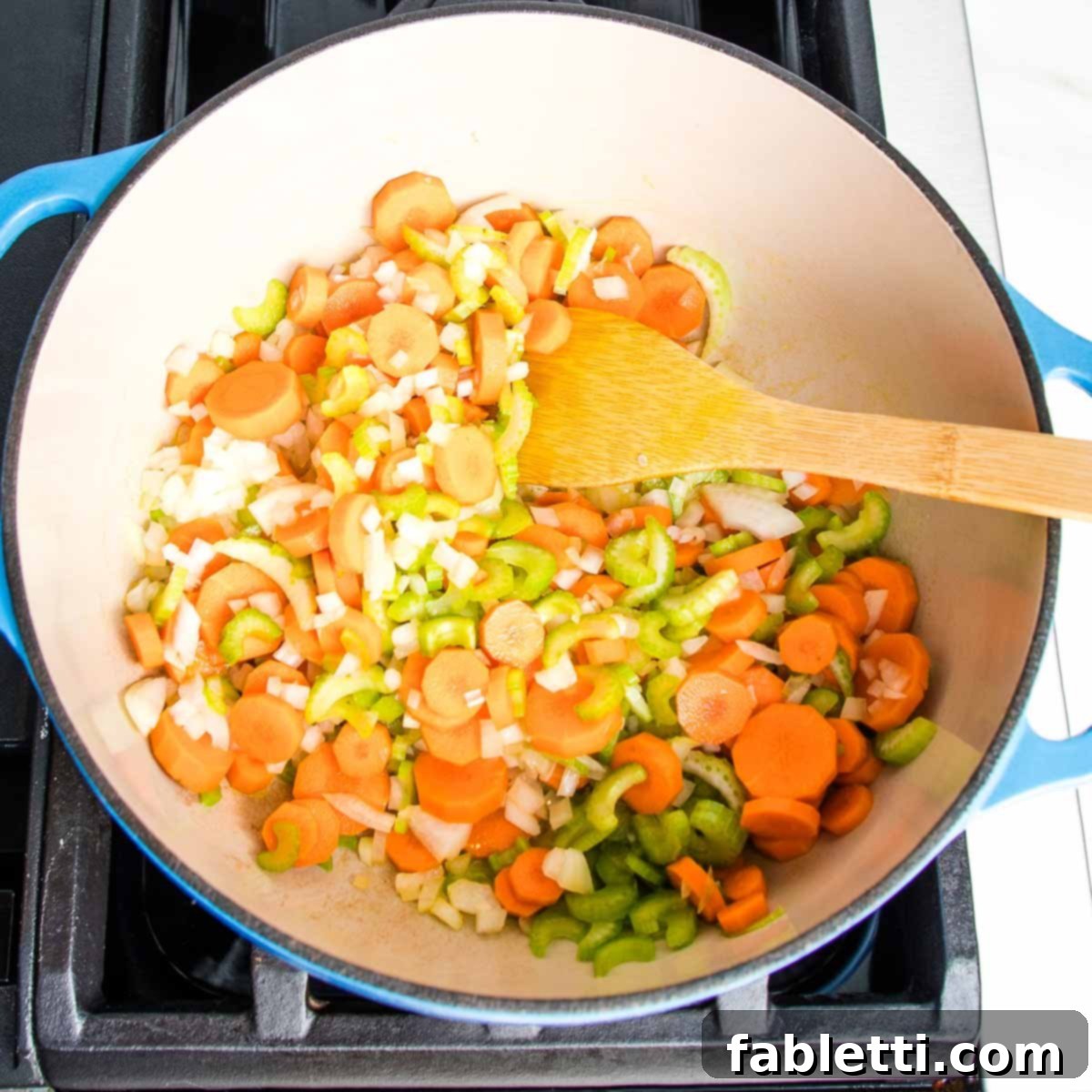 Zesty Vegan Lemon Chickpea Rice Soup 5 Dutch oven filled with chopped carrots, celery, and onions, with a wooden spoon inside.