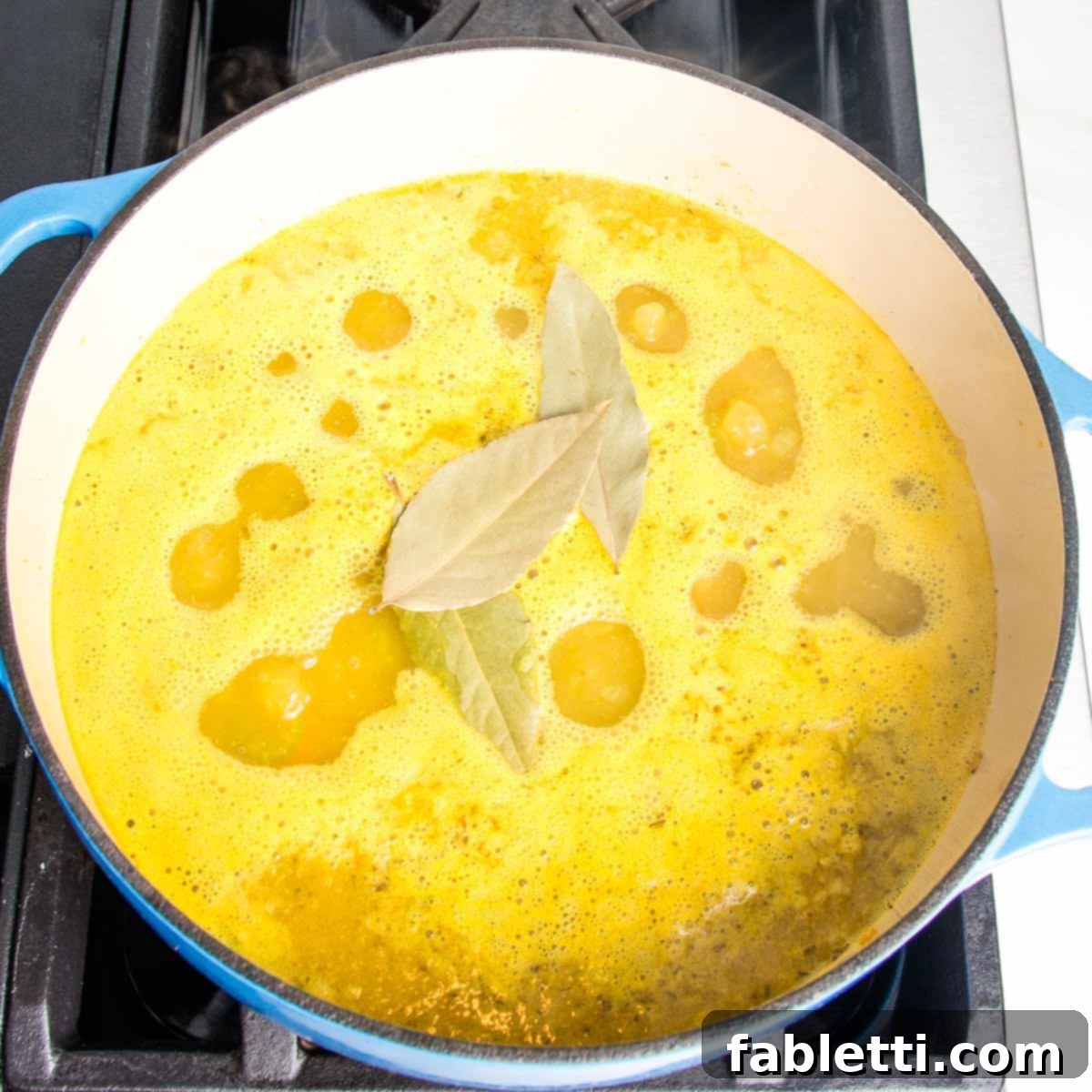 Zesty Vegan Lemon Chickpea Rice Soup 9 Dutch oven with yellow broth and bay leaves during simmering.