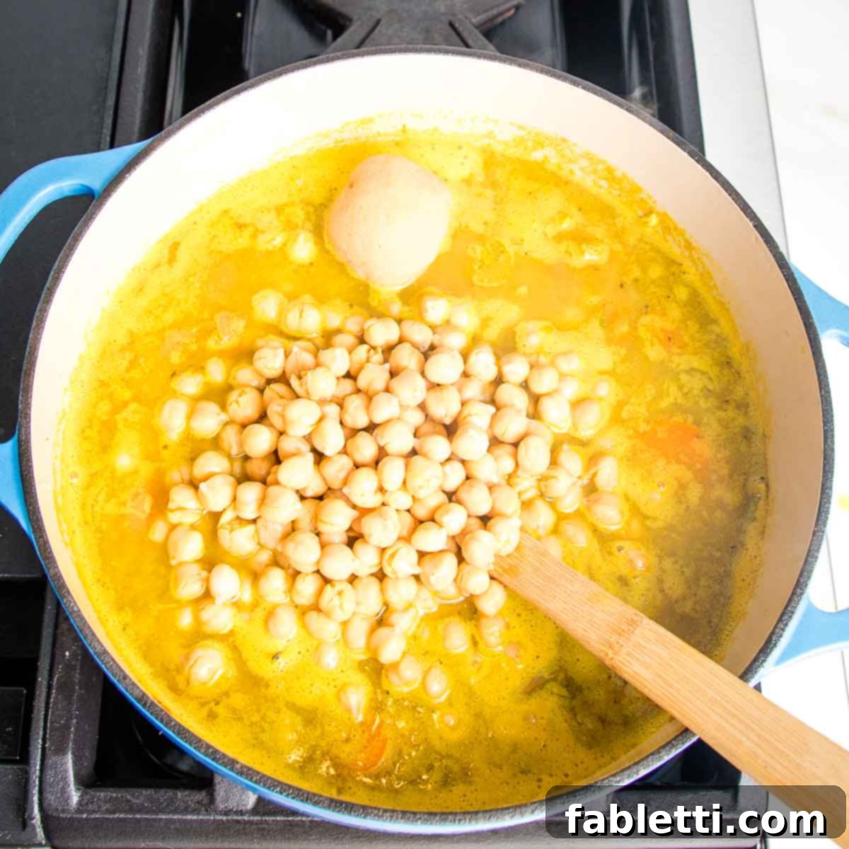 Zesty Vegan Lemon Chickpea Rice Soup 10 Dutch oven with yellow broth, chickpeas, and a scoop of miso paste being added.