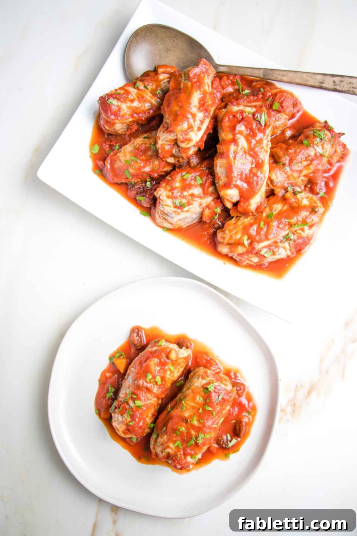 Serving platter of stuffed cabbage rolls with red sauce and a plate with two rolls.