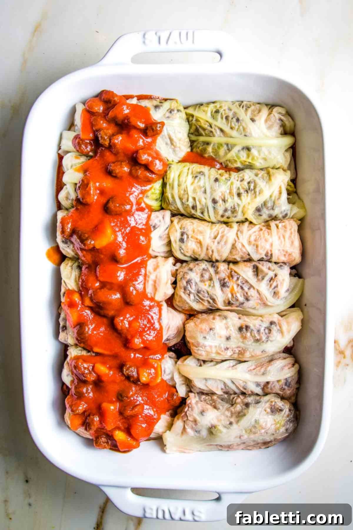Stuffed cabbage rolls on top of sweet and sour sauce in a baking dish, adding more sauce on top.