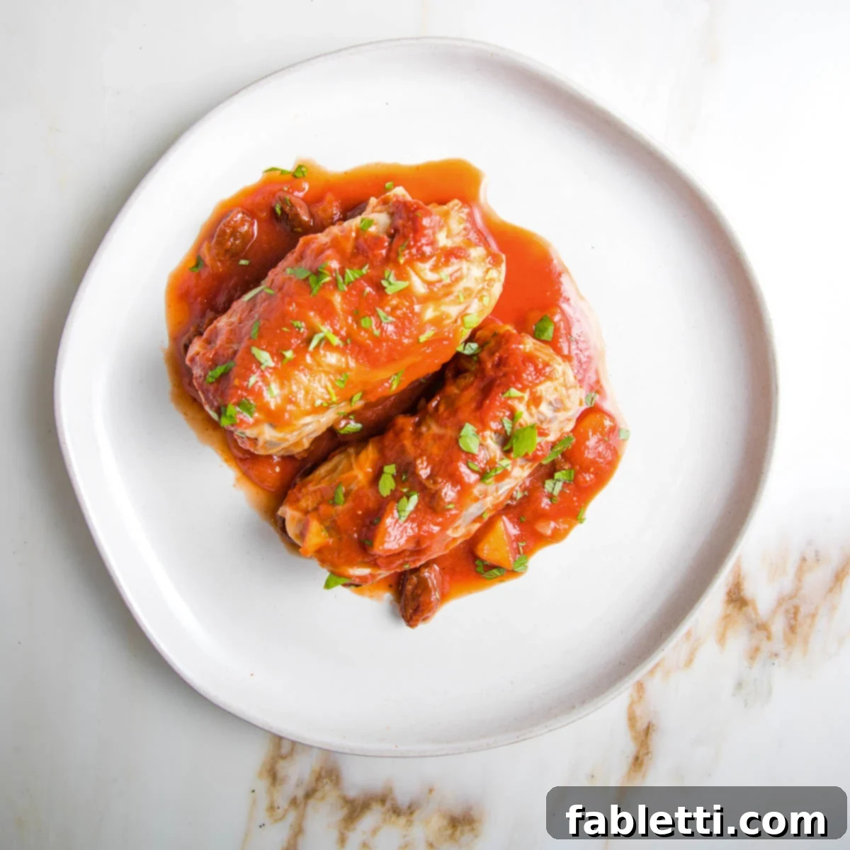 Two stuffed cabbage rolls on a plate with red sauce spooned over.