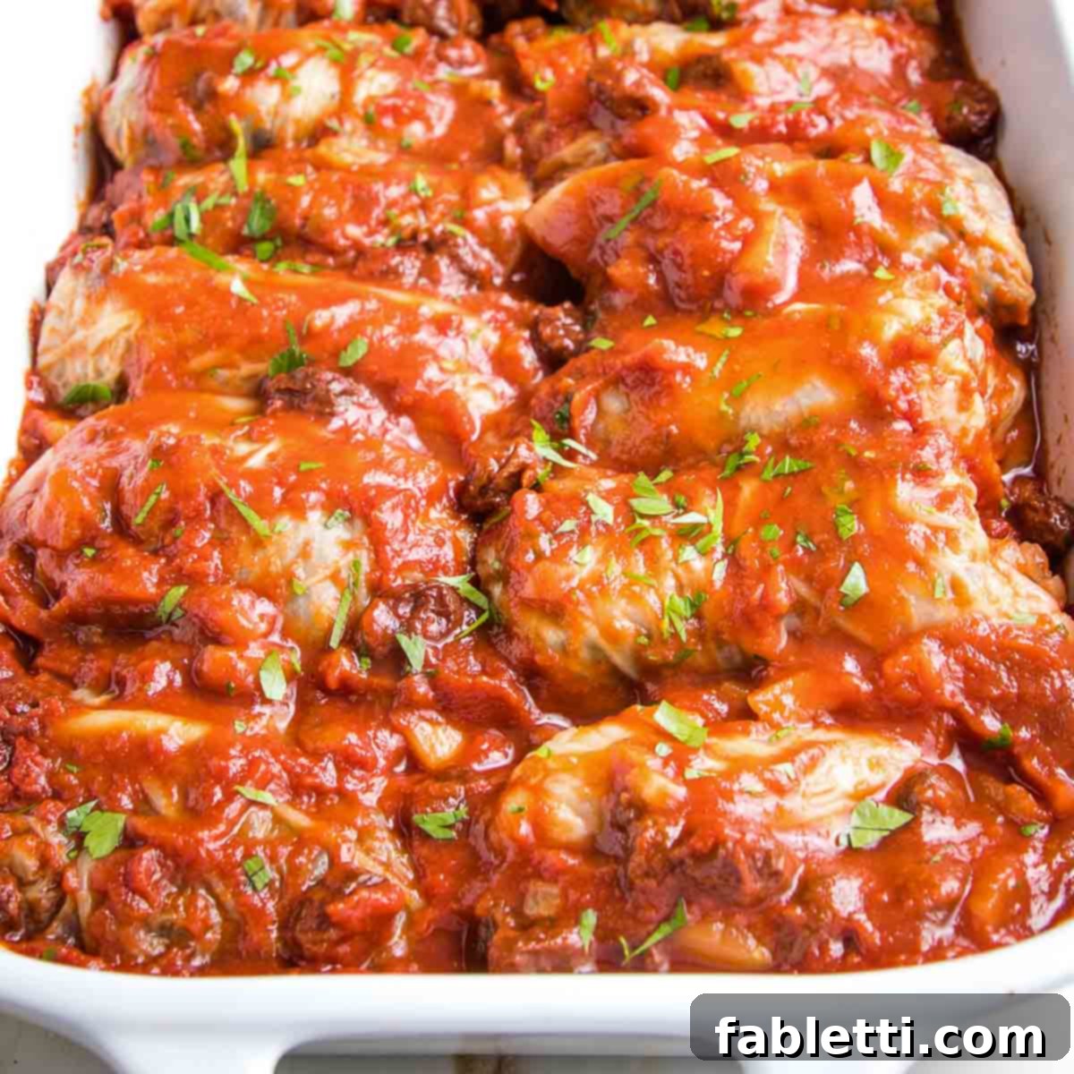 White baking dish with stuffed cabbage in red sauce with fresh herbs on top.