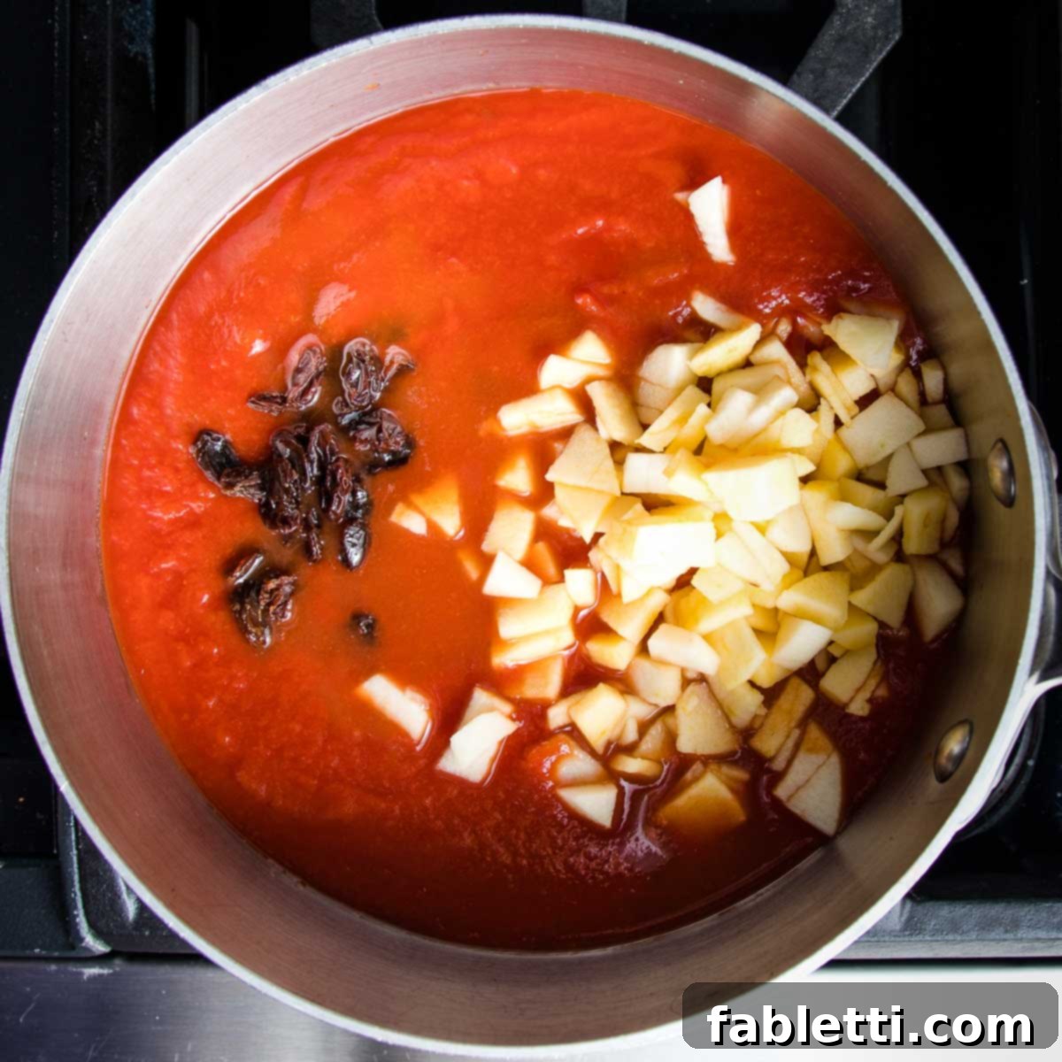 Red sauce in pot with raisins and chopped apple chunks.