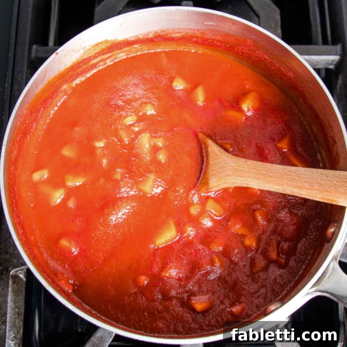 Saucepan with red sauce showing chunks of apples and raisins.
