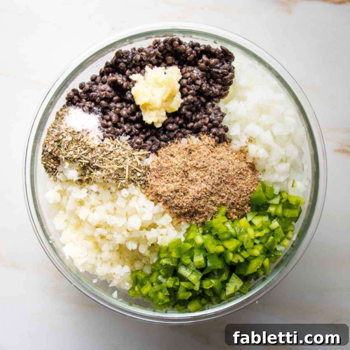 Bowl with sections of diced onions, green peppers, cauliflower rice, ground flax, spices, lentils and pressed garlic.