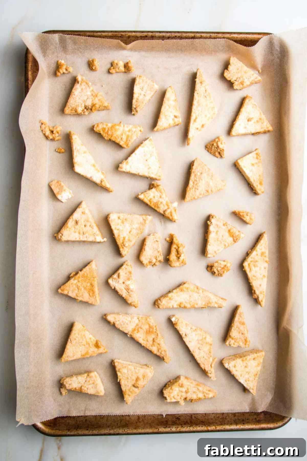 Ultimate Crispy Baked Tofu 11 Small triangles of tofu, spread on a parchment lined baking sheet.