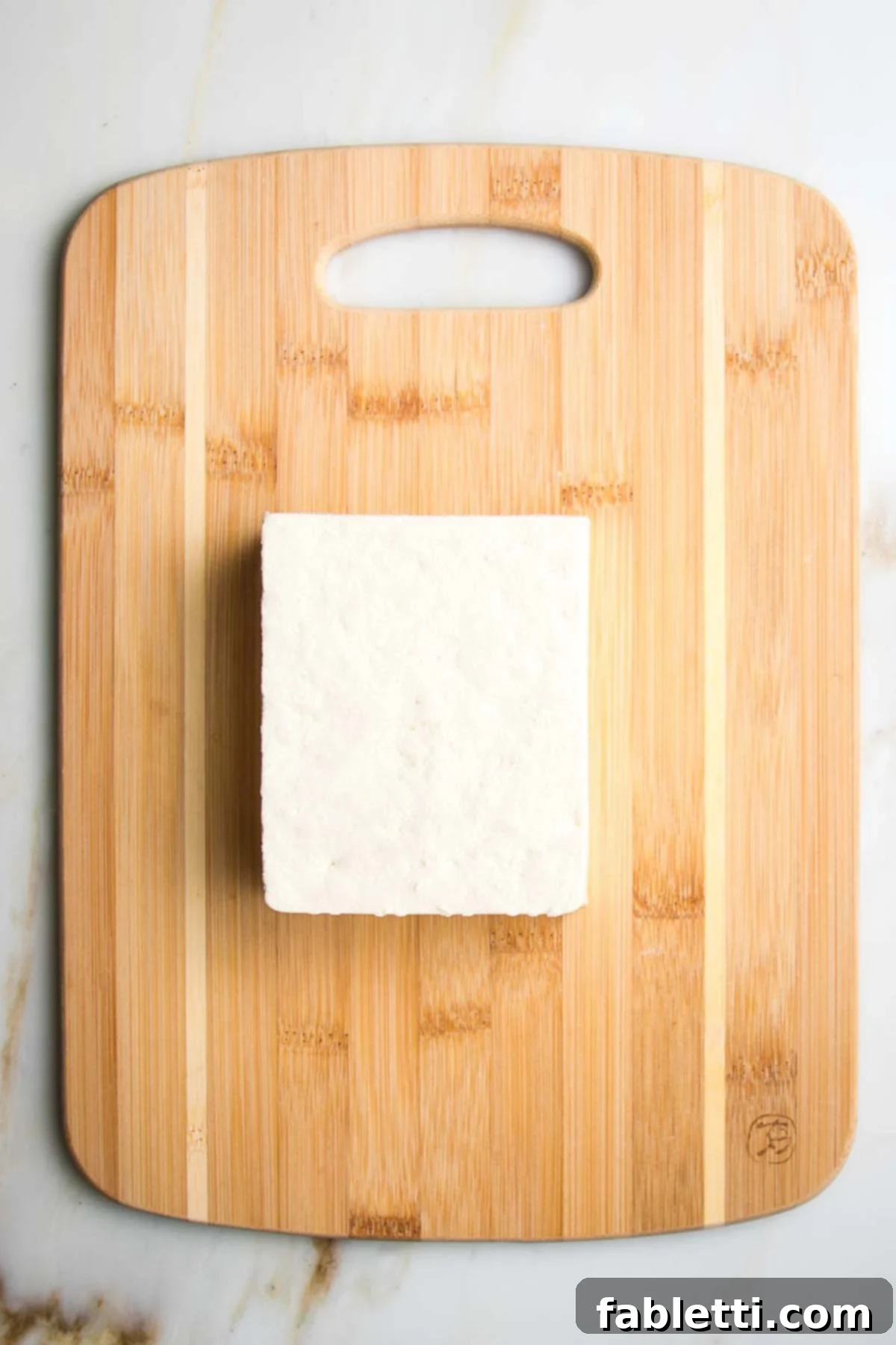 Ultimate Crispy Baked Tofu 3 Block of tofu on a small wooden cutting board.