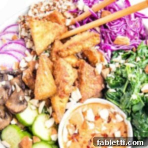 Ultimate Crispy Baked Tofu 20 Crispy tofu pieces in a bowl with brightly colored cooked and raw veggies plus a peanut dipping sauce in a bowl.