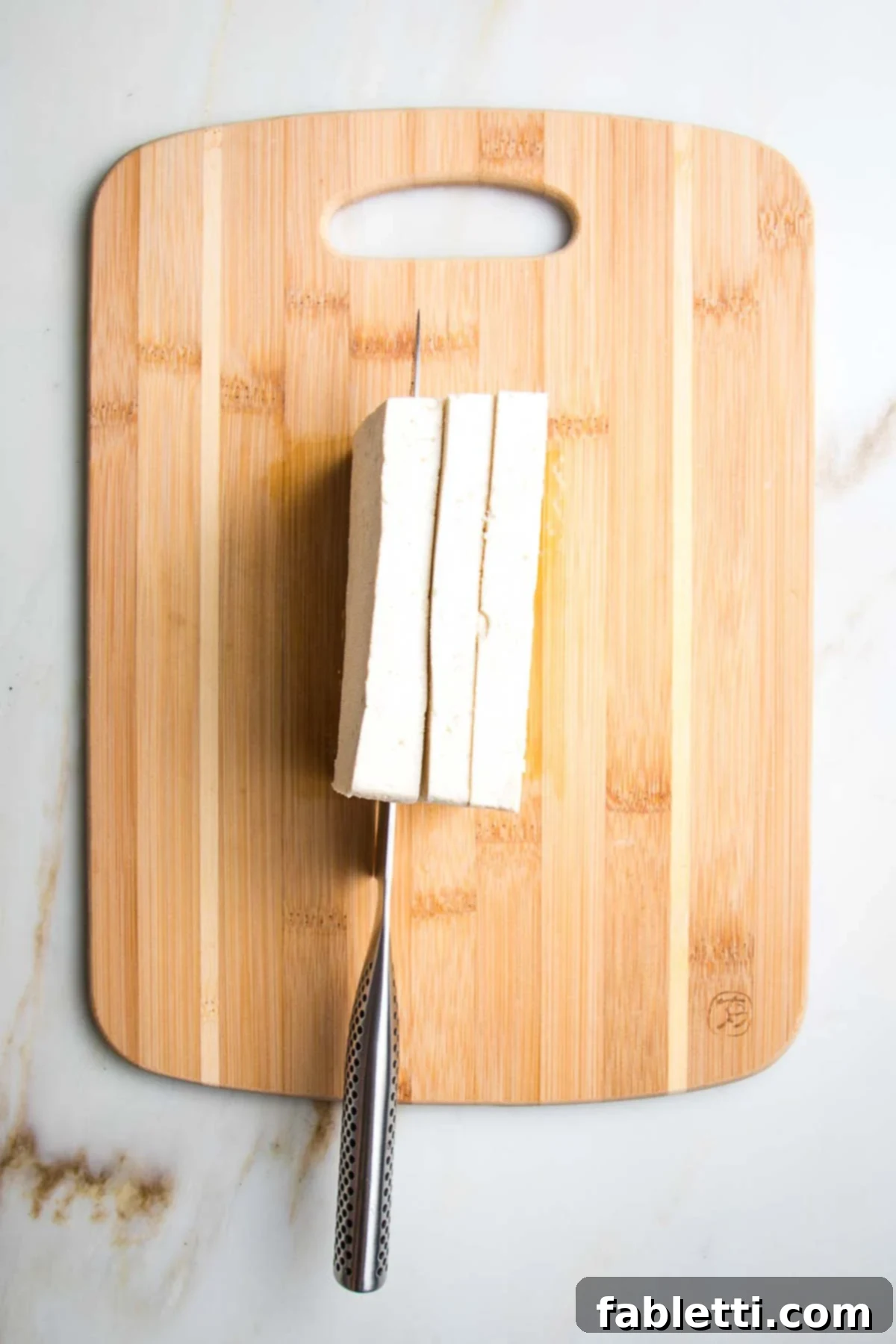 Ultimate Crispy Baked Tofu 4 Block of tofu turned on its side, showing it being cut into 3 equal portions.