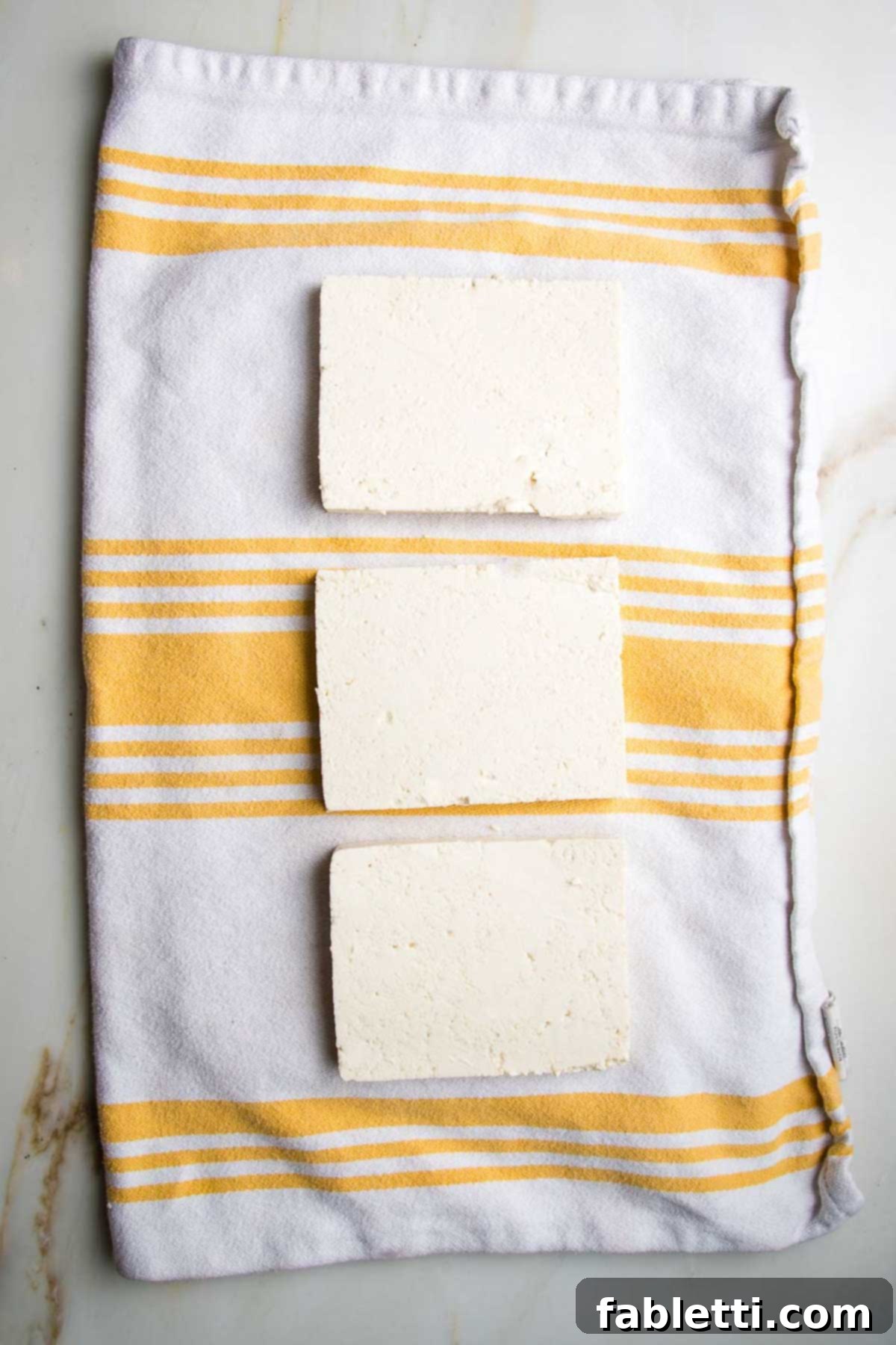 Ultimate Crispy Baked Tofu 5 Three slabs of tofu on a kitchen towel.