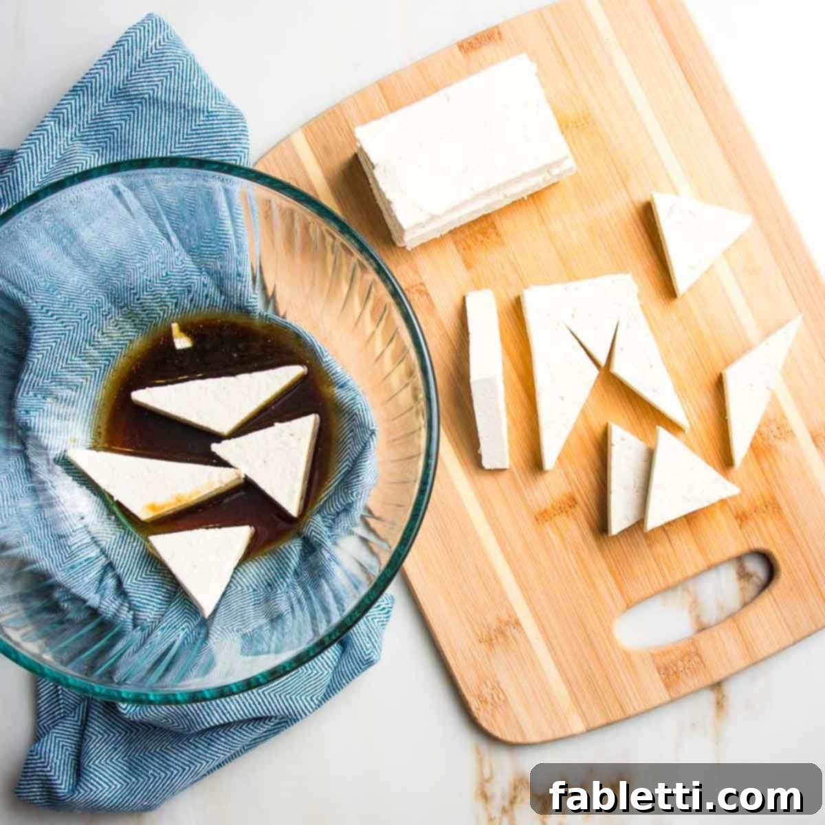 Ultimate Crispy Baked Tofu 8 Cutting small pieces of tofu on a cutting board and then dropping into dark colored marinade in a bowl.