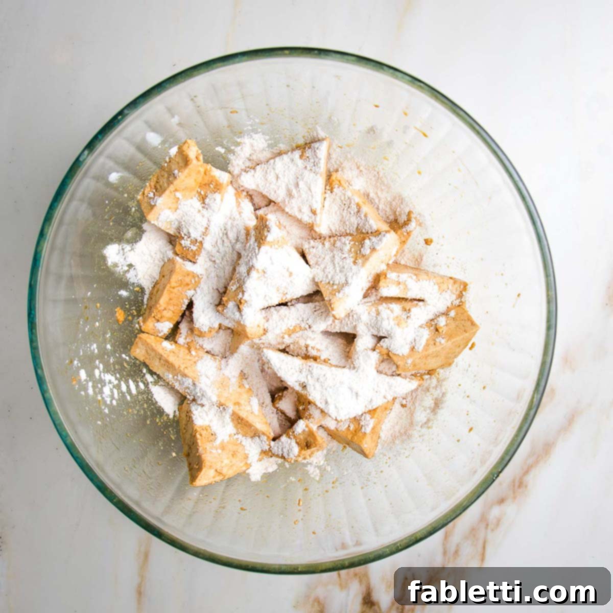 Ultimate Crispy Baked Tofu 9 Triangle pieces of tofu in a bowl, sprinkled with white arrowroot powder.