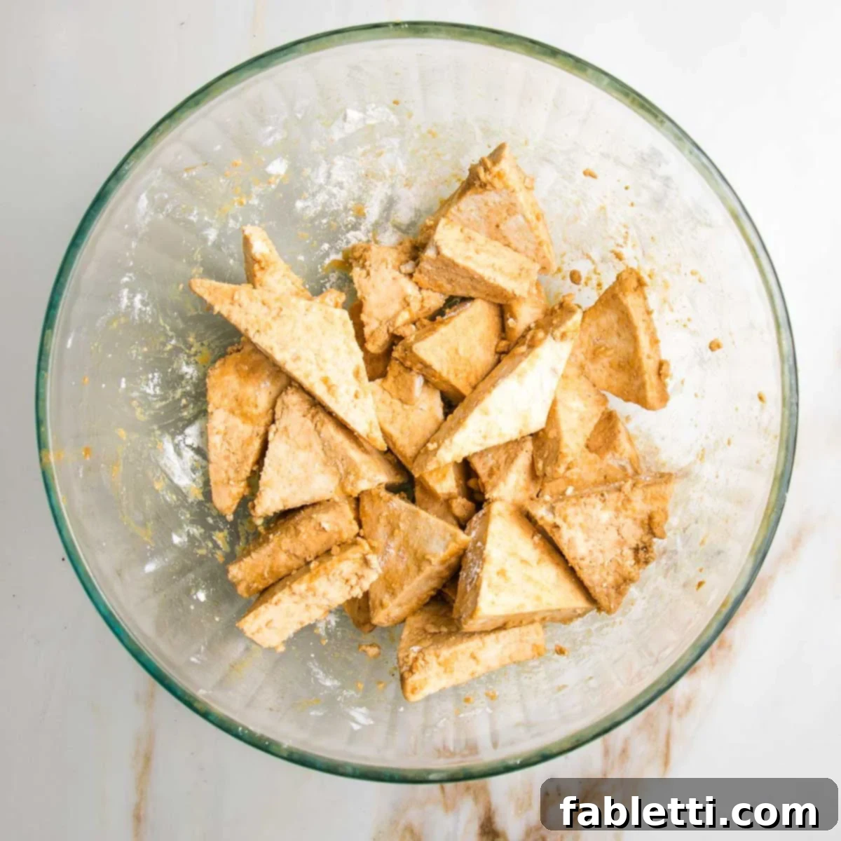 Ultimate Crispy Baked Tofu 10 Small, triangle pieces of tofu with marinade and arrowroot in a bowl..