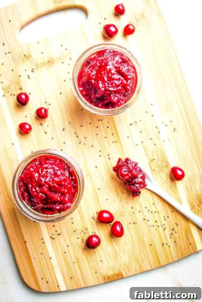 Naturally Sweetened Cranberry Chia Jam 2 Two small glass jars with cranberry jam, a few cranberries on the sides plus a spoonful of jam.