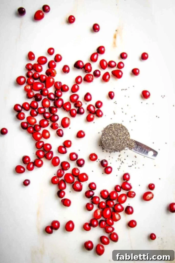 Naturally Sweetened Cranberry Chia Jam 4 Cranberries spread out on a white counter along with a tablespoon filled with chia seeds.