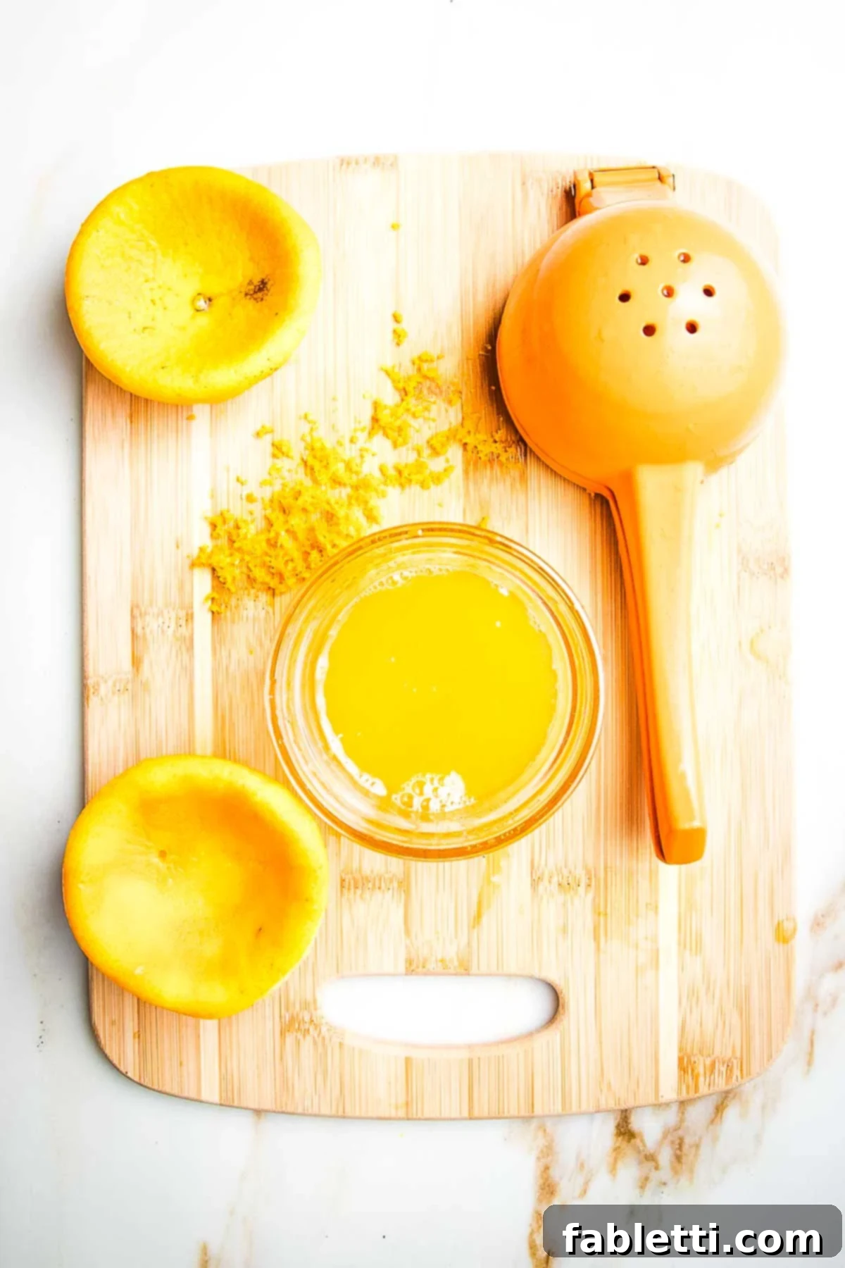 Naturally Sweetened Cranberry Chia Jam 6 Orange that's been zested and juiced, the squished orange halves still on the cutting board along with the juicer, a dish of the juice and zest on the cutting board.