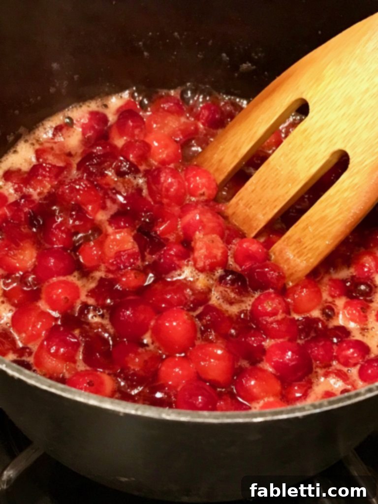 Naturally Sweetened Cranberry Chia Jam 7 Saucepan with cranberries foaming as they cook, a wooden spatula is stirring them.