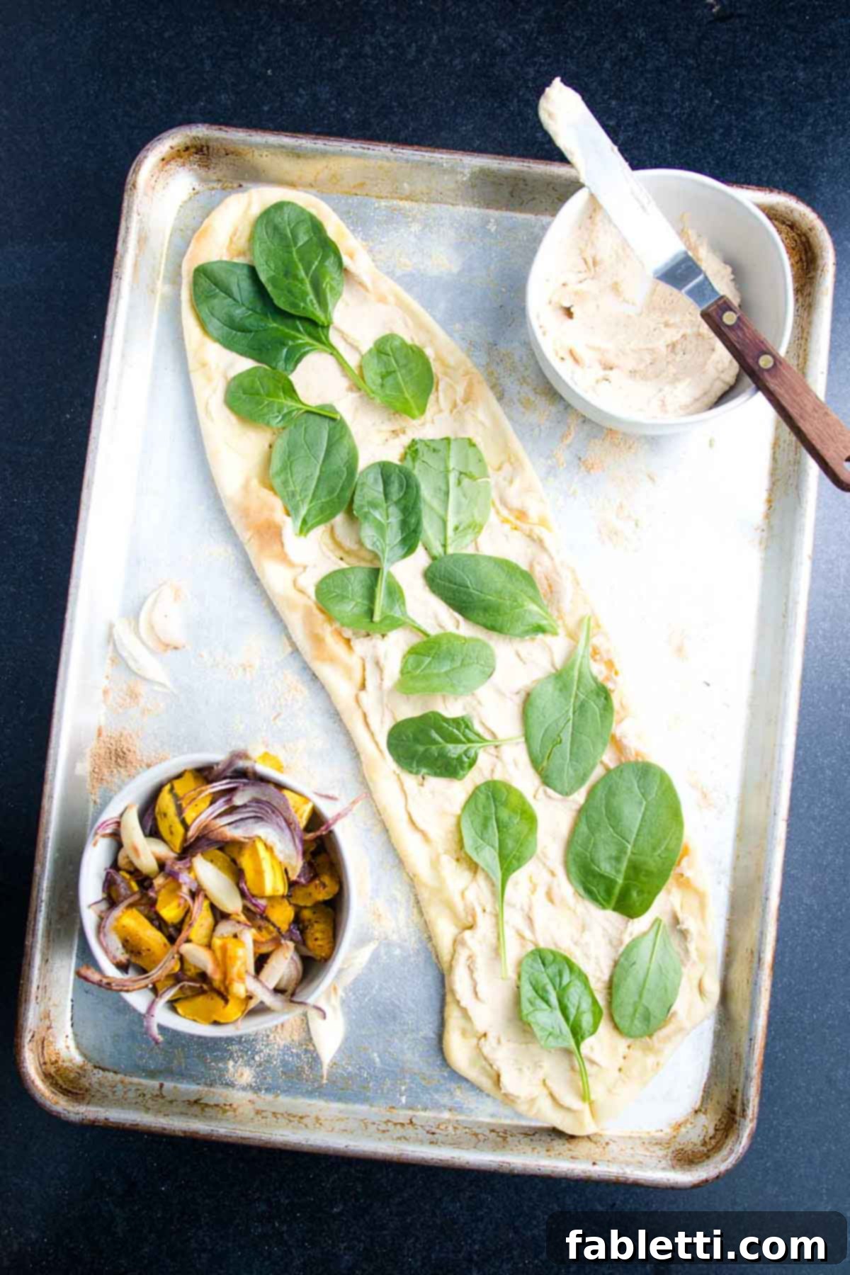 Effortless Plant-Based Flatbread 14 Flatbread pizza spread with hummus and topped with fresh spinach.