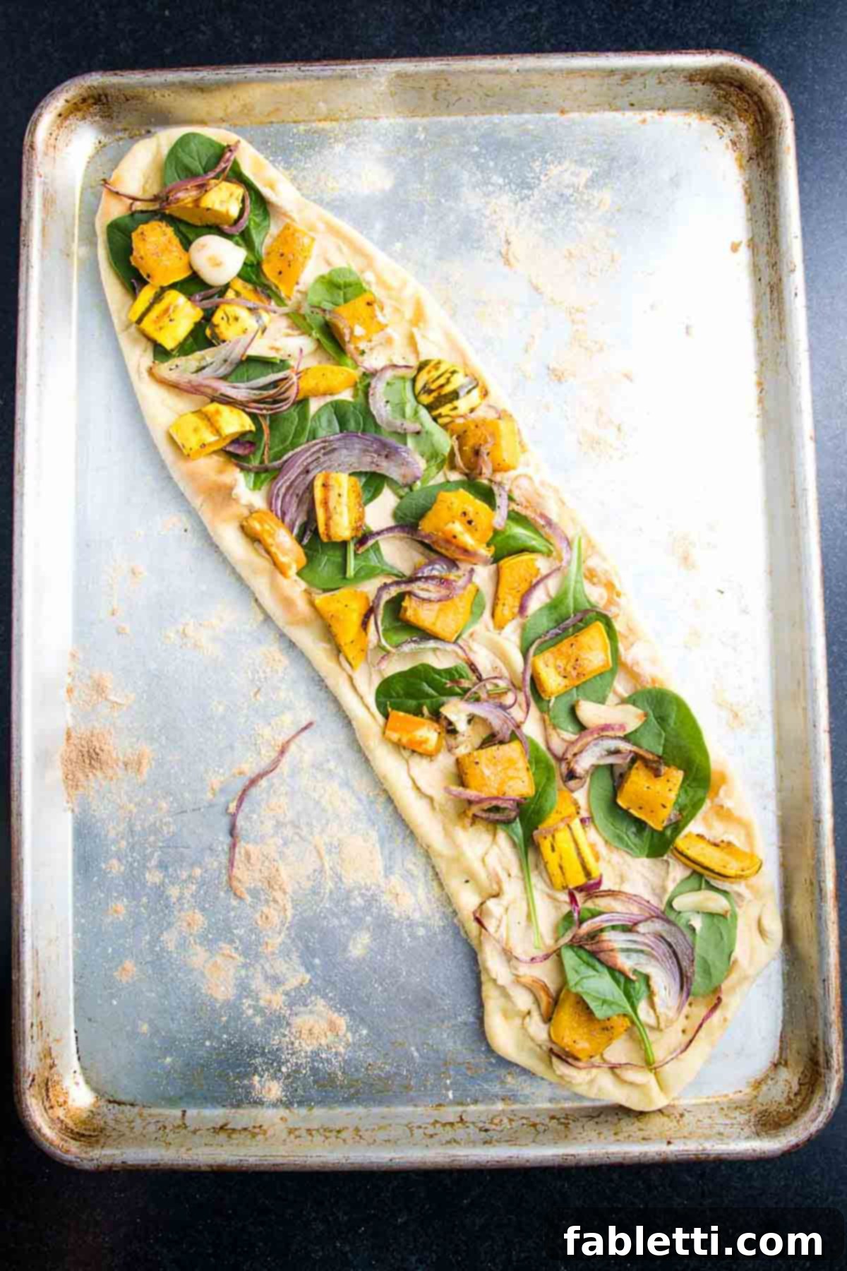 Effortless Plant-Based Flatbread 15 Flatbread pizza spread with hummus and topped with fresh spinach.