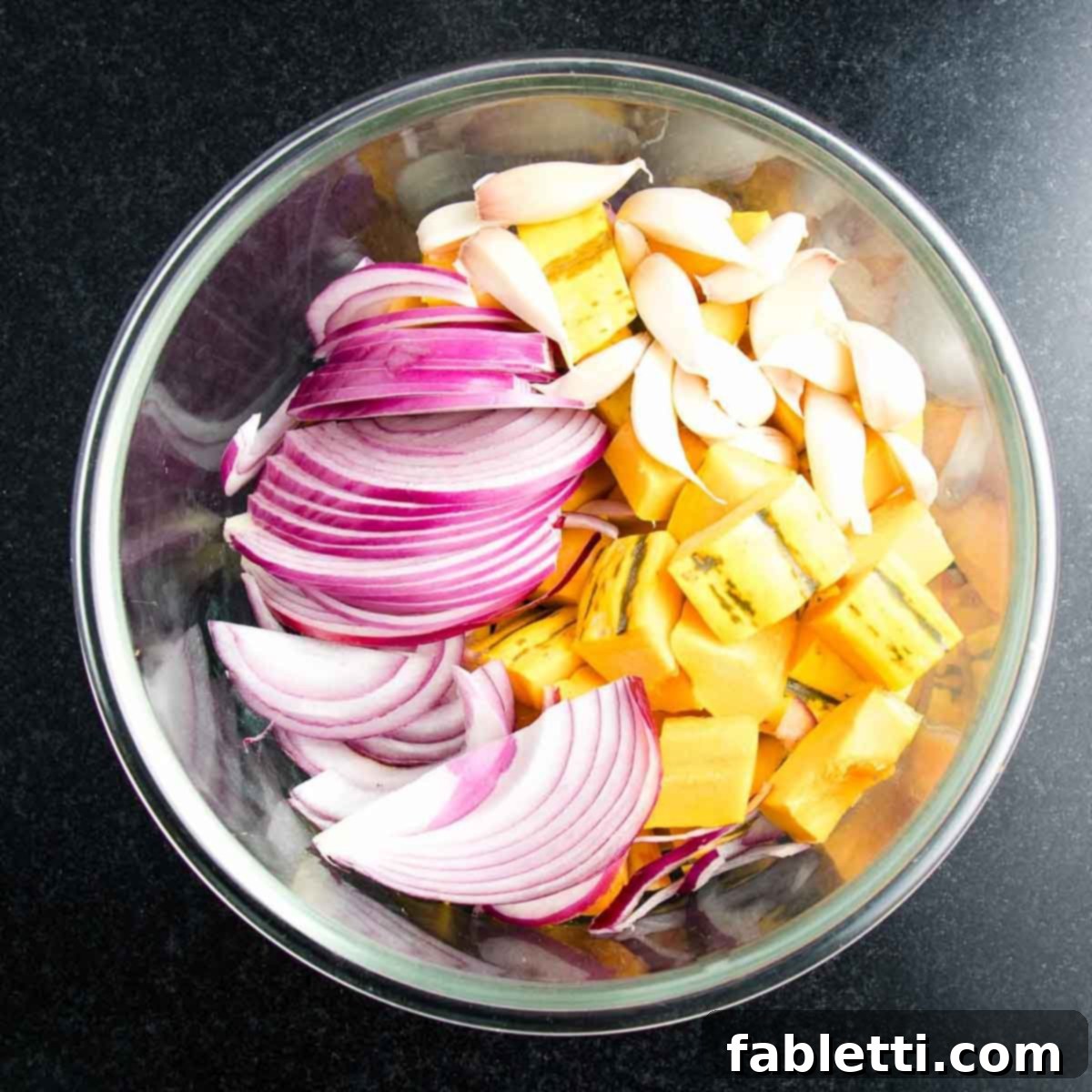 Effortless Plant-Based Flatbread 20 Bowl with cubes of squash, thinly sliced onions and cloves of garlic.