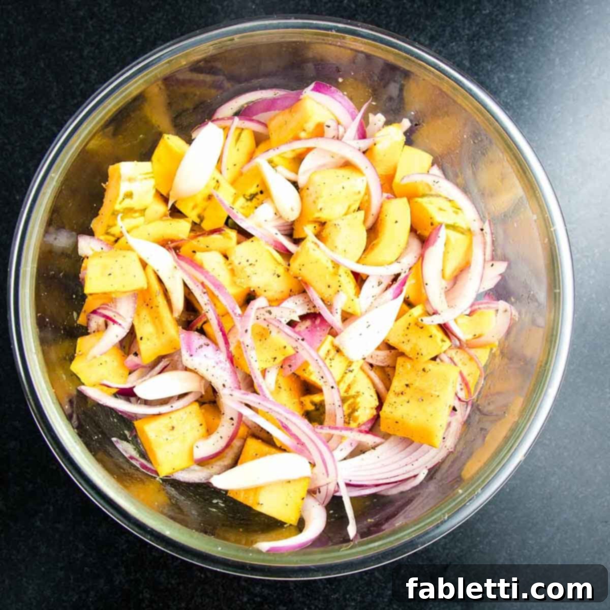 Effortless Plant-Based Flatbread 21 Bowl with cubes of squash, thinly sliced onions and cloves of garlic, drizzled with olive oil.