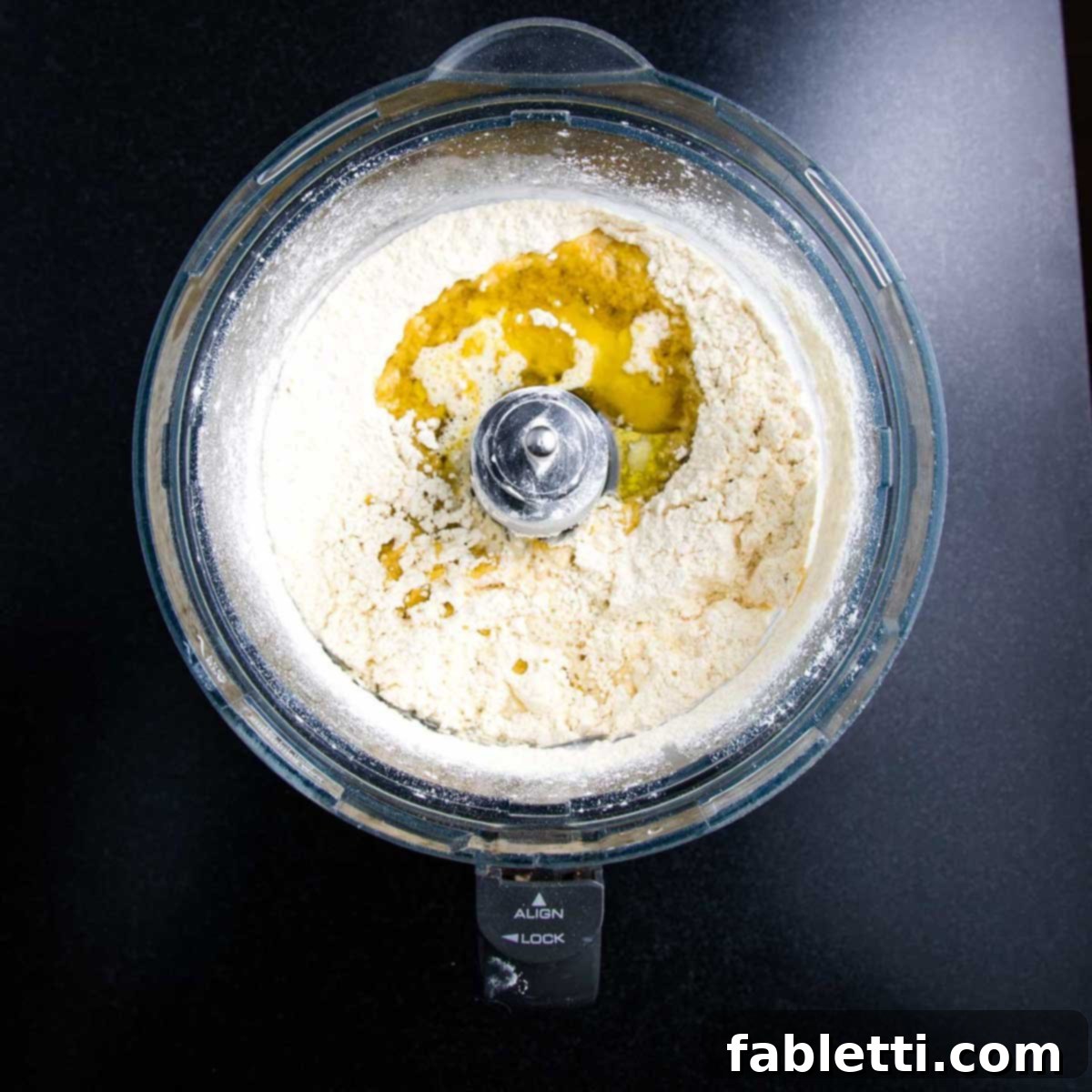 Effortless Plant-Based Flatbread 4 Oil and water poured onto a food processor bowl filled with flour and water.