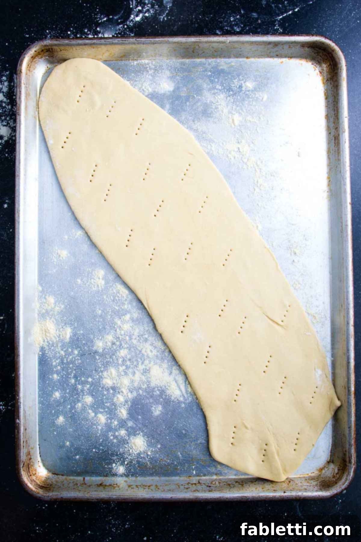 Effortless Plant-Based Flatbread 10 Long, thin oval of pizza dough on a baking sheet, with fork marks.