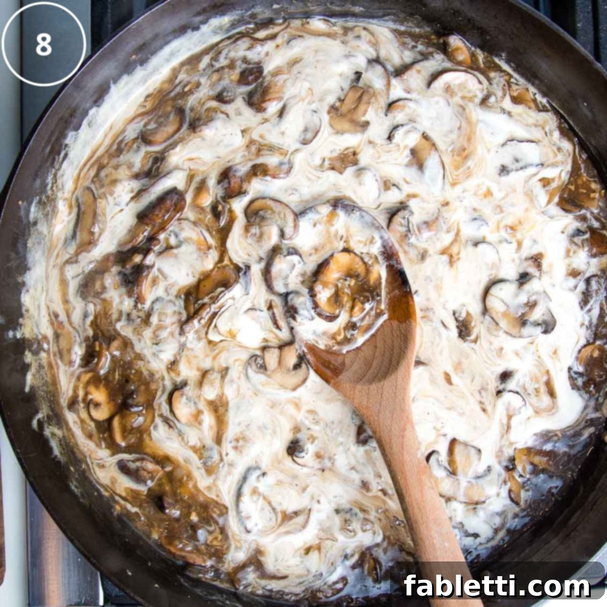 Hearty Vegan Mushroom Stroganoff 12 Vegan sour cream being gently stirred into the rich mushroom sauce in a cast iron skillet, creating a creamy swirl.