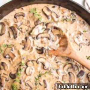 Hearty Vegan Mushroom Stroganoff 16 Close up of cast iron skillet filled with creamy vegan sauce, loaded with sliced mushroom, fresh thyme and a wooden spoon stirring it.