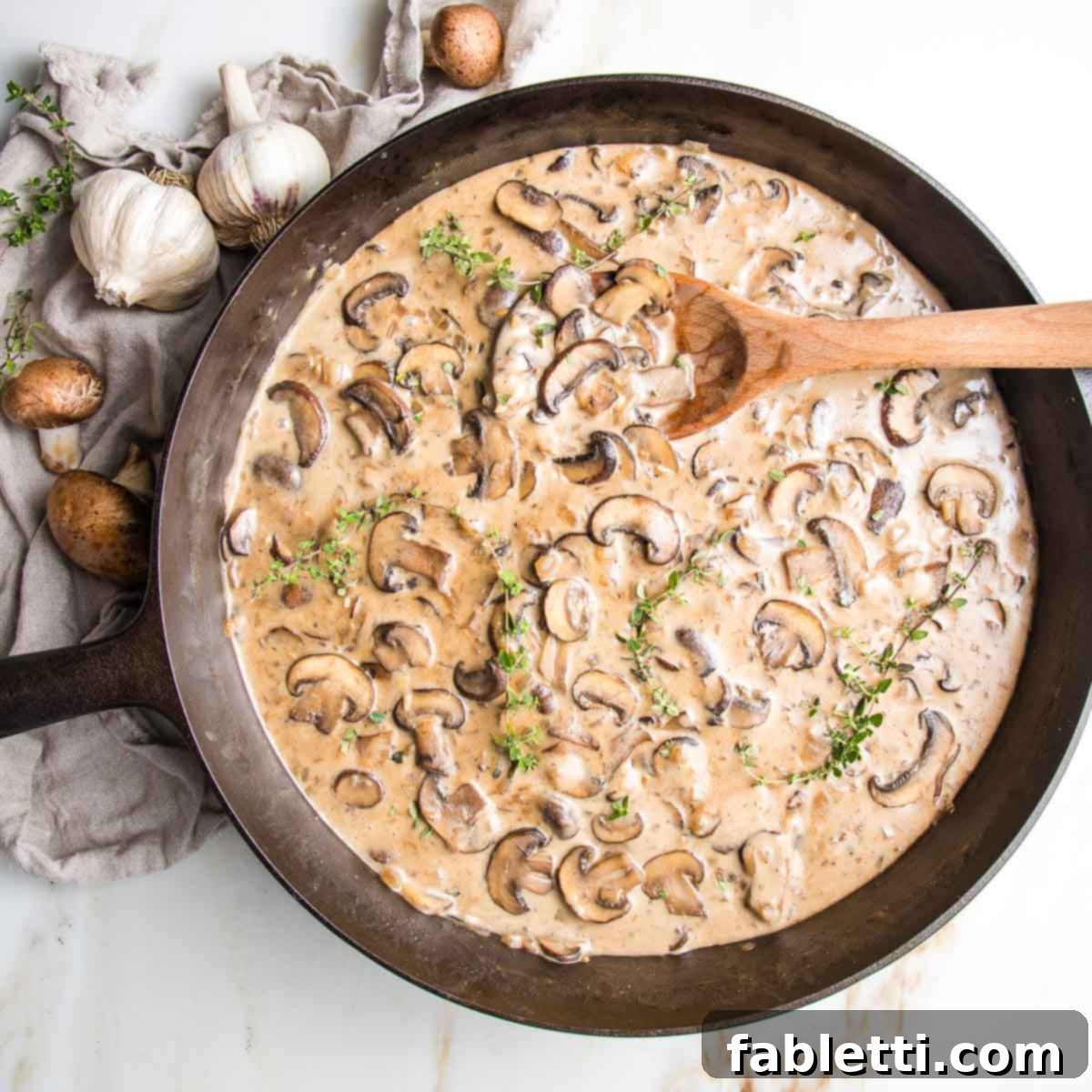 Hearty Vegan Mushroom Stroganoff 3 Close-up of sliced mushrooms simmering in a creamy brown sauce within a cast iron skillet, hinting at rich flavors.
