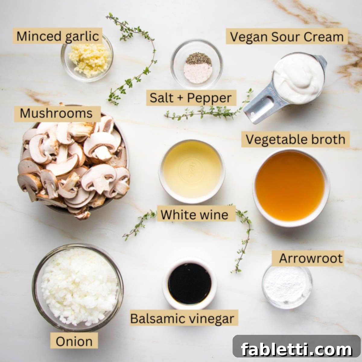 Hearty Vegan Mushroom Stroganoff 4 Carefully arranged ingredients for vegan mushroom stroganoff: minced garlic, vegan sour cream, fresh mushrooms, vegetable broth, white wine, diced onion, balsamic vinegar, and arrowroot powder.
