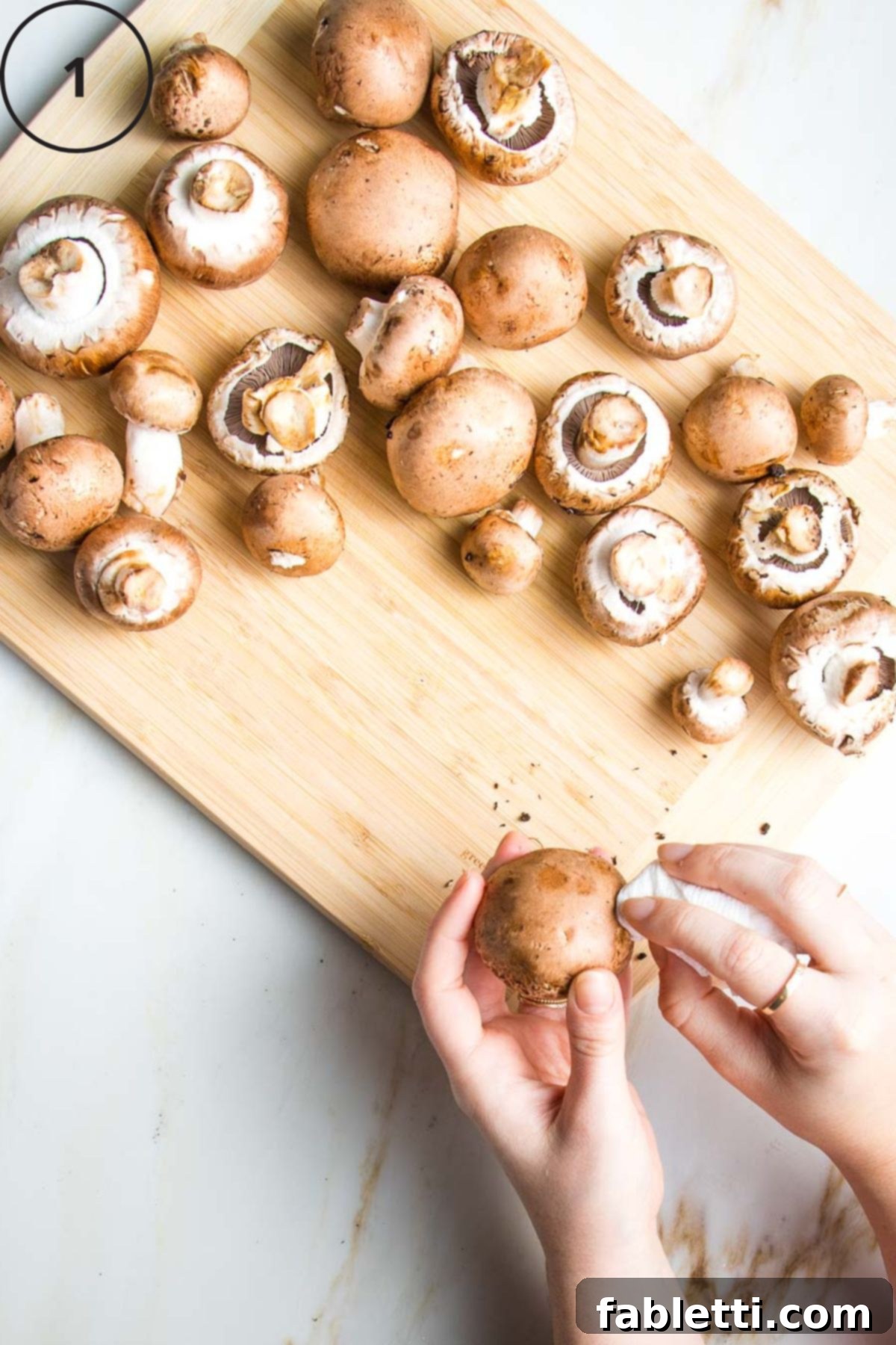 Hearty Vegan Mushroom Stroganoff 5 Demonstration of cleaning dirt off baby bella mushrooms with a damp paper towel to prepare them for cooking.